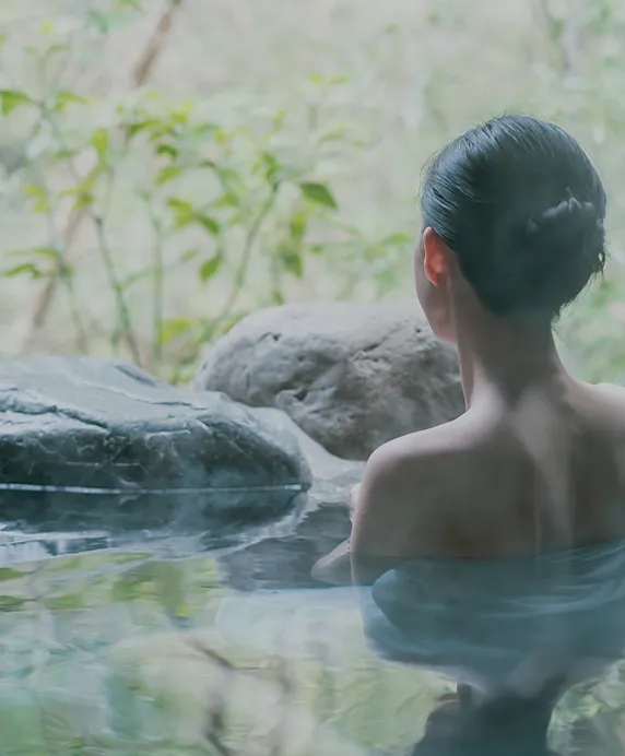 岩に囲まれた露天風呂に入る女性の後ろ姿